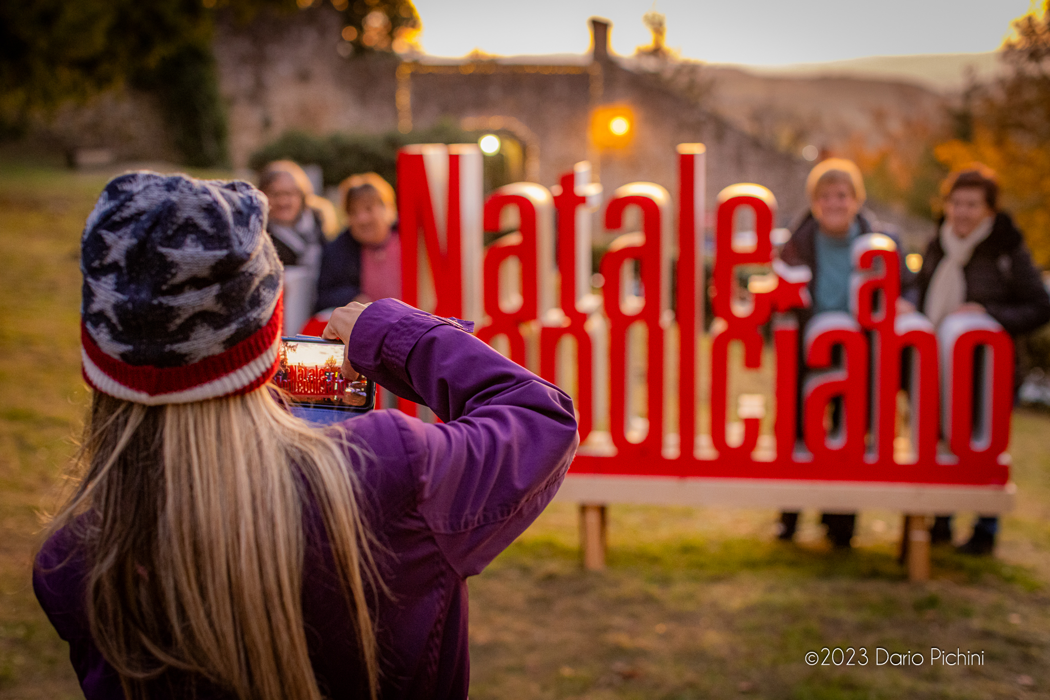 Una signora fa una foto al cartello di colore rosso Natale a Montepulciano